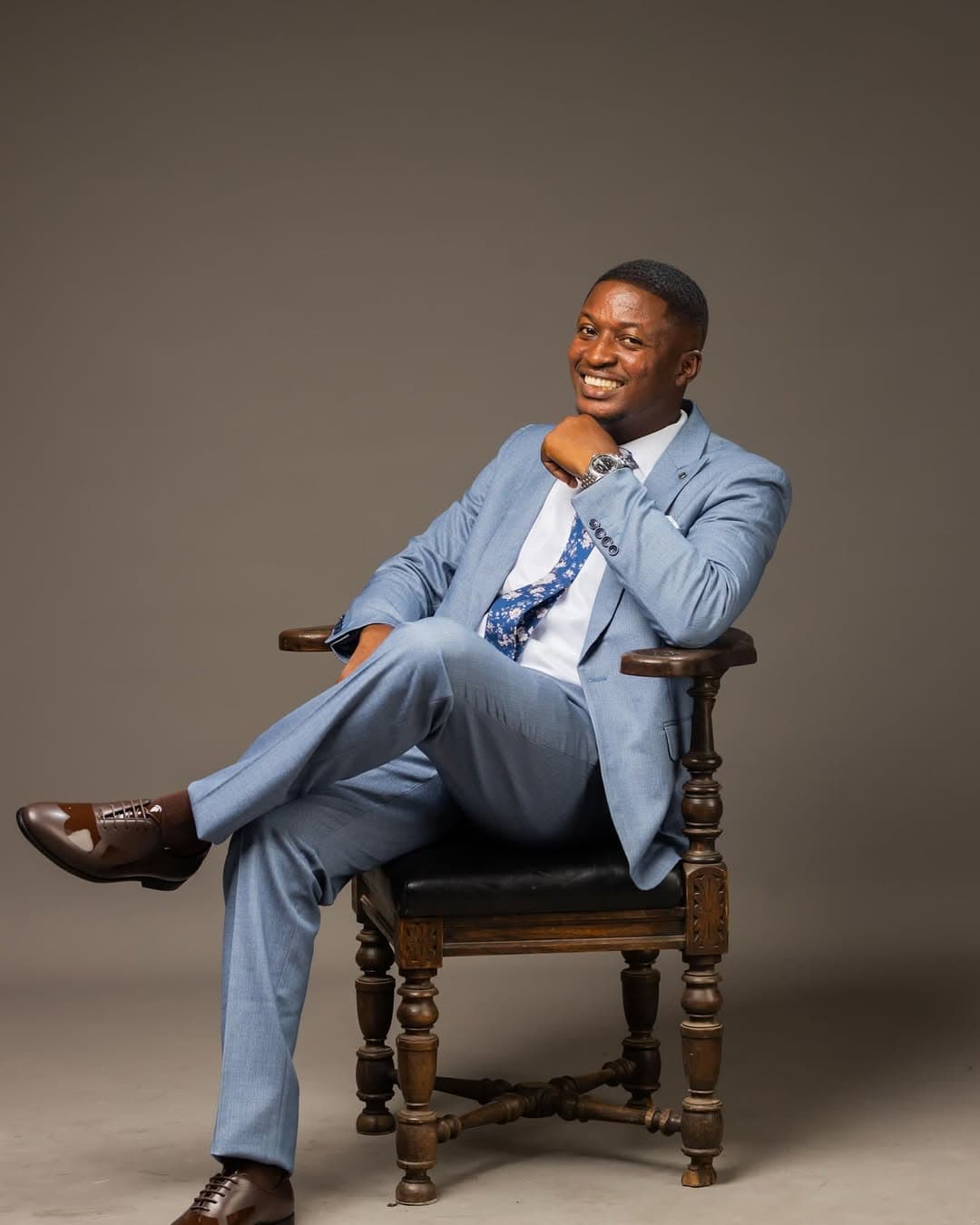 Minister Theophilus Badger in professional light blue suit sitting in ornate wooden chair, smiling warmly