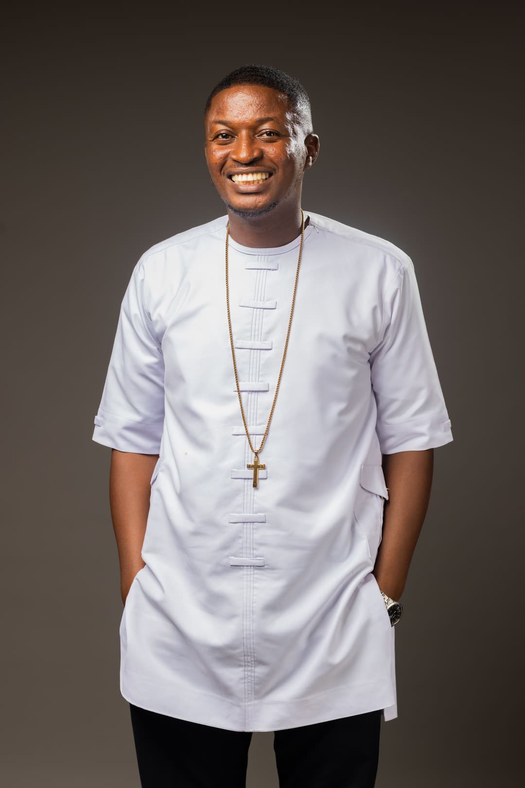 Rev. Theophilus Badger in professional white attire with gold cross necklace, smiling warmly